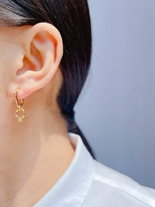 Close-up of gold C-shaped hoop earring with a zircon-set ring pendant on a model