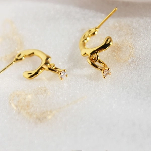 Elegant gold C-shaped earrings with sparkling zircon pendant on soft white texture