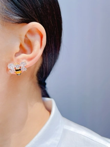 Close-up of handmade enamel bee stud earring with zircon wings on a model's ear