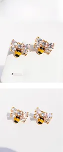 Detail of bee earrings with gold base, white zircon wings and yellow black enamel finish