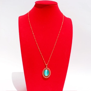 Collier doré avec pendentif ovale vert émeraude et zircons sur buste en velours rouge