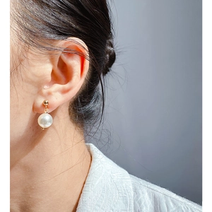 Elegant white pearl earrings with gold spherical hooks worn by a model in close-up