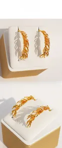 Detailed view of gold feather-shaped earrings with intricate textures and artistic shadows