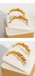 Close-up of golden feather earrings with wheat spike texture on white jewelry card