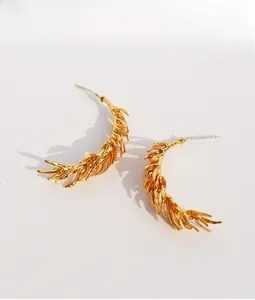 Macro detail of golden feather leaf earrings showing intricate metal texture and finish