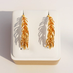 Golden feather drop earrings with textured leaf design on a white jewelry display stand