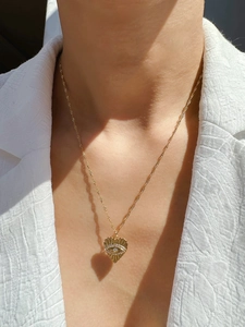 Détail d'un collier pendentif cœur doré avec motif œil protecteur porté au cou