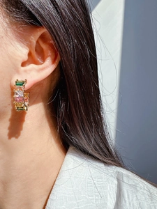Macro shot of C-shaped gold earrings set with colorful rectangular cubic zirconia stones