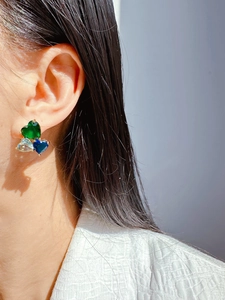 Close-up of triple heart earrings with blue and green crystals on a gold setting