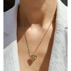Collier pendentif cœur doré avec détail œil et cristaux blancs porté par un mannequin