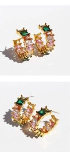 Macro shot of gold C-shaped earrings with colorful square-cut rainbow cubic zirconia