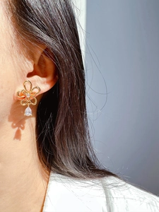 Close-up of a gold hollow flower earring with a pear-cut crystal drop on a model