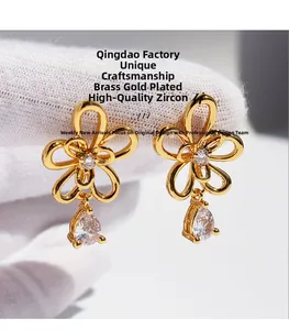 Detailed close-up of gold-plated flower earrings with teardrop zircon held by hand