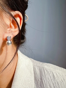 Detail of gray pearl earring with round cut gemstone worn on model's earlobe