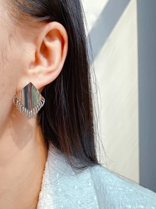Close-up of silver geometric diamond-shaped earrings with tassel fringe on a model