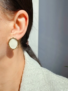 Detail van elegante gouden oorbellen met wit emaille op model in tweed jasje