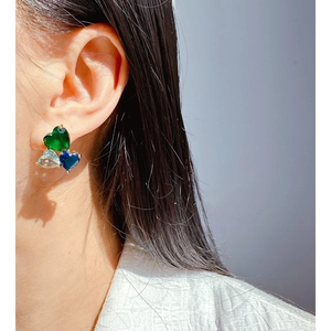 Three heart-shaped blue and green zircon stud earrings shown on a model's ear