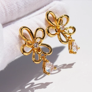 Elegant gold hollow flower earrings with water drop zircon stone on white background