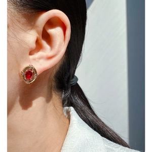 Vintage oval red zircon earrings with gold sunburst texture worn on a model ear