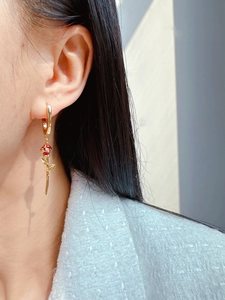 Detail view of red enamel rose earrings with gold U-shaped hoops on a female model