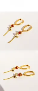 Detail of U-shaped gold earrings with red enamel rose pendant and textured metal leaves