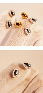 Close-up of polished gold and silver minimalist bean-shaped stud earrings on white glove
