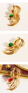 Detailed view of golden phoenix brooch featuring emerald and ruby teardrop gemstones