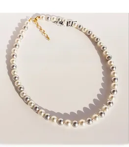 Détail d'un collier de perles grises et blanches avec fermoir en laiton doré et zircon