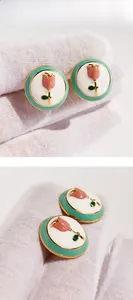 Detail of pink enamel tulip stud earrings with gold trim held on a white glove