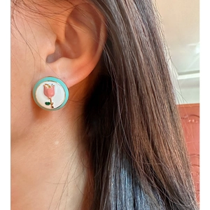 Pink enamel tulip round stud earrings with mint green border worn on model's ear