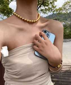 Detail of elegant gold pearl necklace and obsidian bracelet worn by a model in a garden