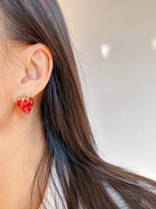 Close-up of a realistic red enamel strawberry earring with golden leaves on ear