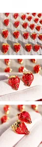 Detail of red enamel strawberry earrings with golden leaves and pink rhinestones