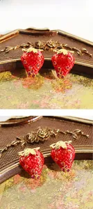 Detailed macro view of red enamel strawberry earrings with sparkling purple zircons