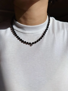Dettaglio di una collana minimalista di perle nere con pendente a sfera d'argento su modella