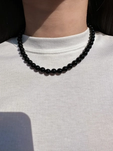 Close-up of polished black round beaded necklace on model with white ribbed shirt
