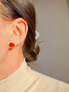 Close-up of minimalist red enamel cherry-shaped stud earrings worn by a model