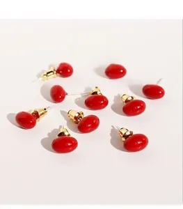 Detailed macro shot of red enamel cherry stud earrings with gold-plated brass texture