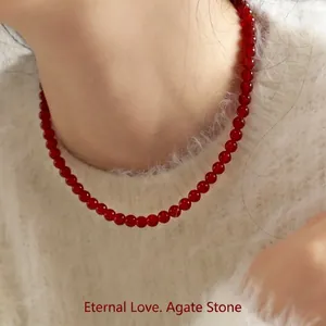 Red agate bead necklace with gold clasp on model wearing white knit sweater