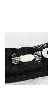 Macro shot of silver enamel candy-shaped brooch on black knit and white paper texture