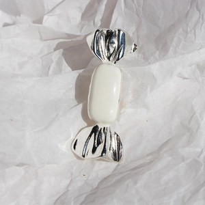 Silver candy brooch with white enamel finish on textured paper background for fashion styling