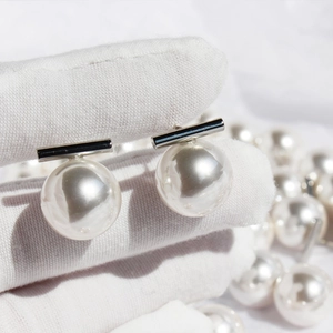 Minimalist geometric pearl stud earrings with black metal bar on a blurry pearl background