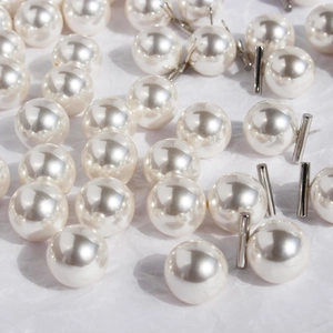 Lustrous white pearl stud earrings with silver metal posts on a textured paper background