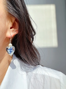 Detail of heart earring featuring blue white porcelain pattern and glossy pearl on model