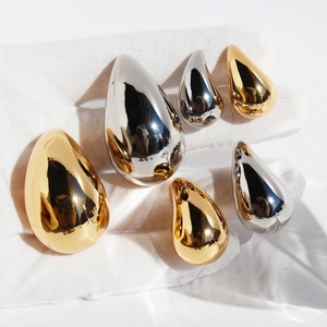 Polished mirror-finish gold and silver teardrop earrings held in a hand on white background