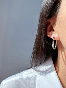 Macro shot of silver U-shaped earrings with colorful pave-set zircon stones on earlobe