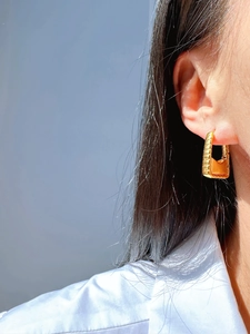 Detailed close-up of a 24k gold plated earring in a textured handbag shape on a model