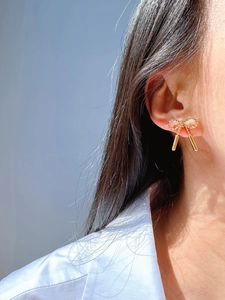 Close-up of model wearing golden bow stud earrings with twisted rope design and pendants