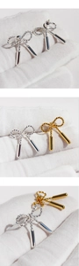 Macro detail of twisted bow earrings with polished drop tassels in gold and silver