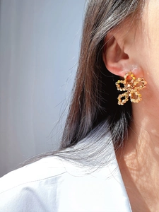 Close-up of golden handmade woven metal petal earrings worn on ear with artistic shadows